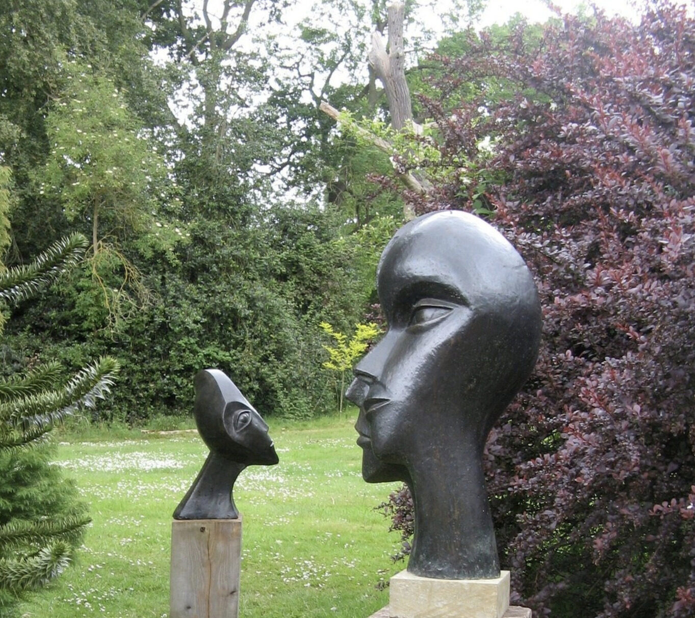 contemporary bronze sculptures of double heads installed in the garden